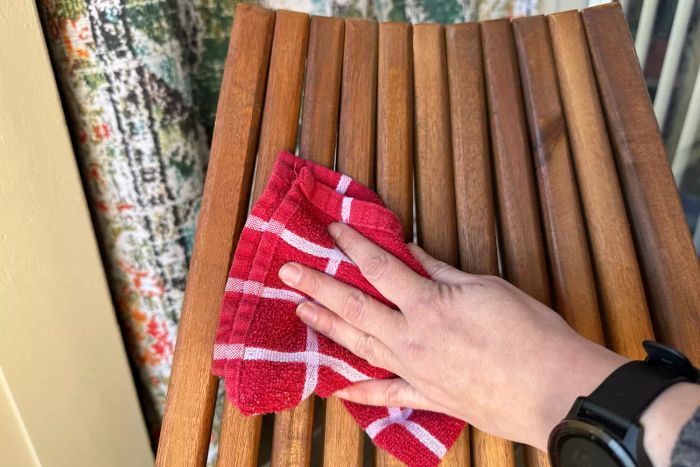 A hand wiping the Sand and Stable Abingdon Wood Folding Adirondack Chair with a red towel.
