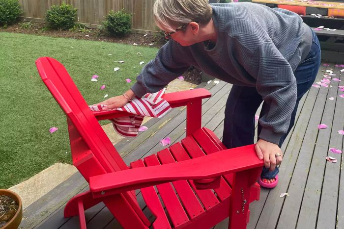 A person is wiping down the Ciokea Folding Adirondack Chair with a towel.