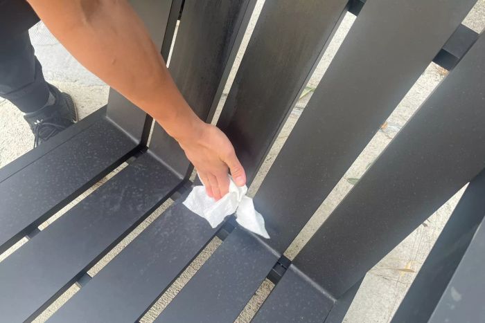 A person is seen wiping down the Pottery Barn Malibu Metal Adirondack Outdoor Lounge Chair using a paper towel.
