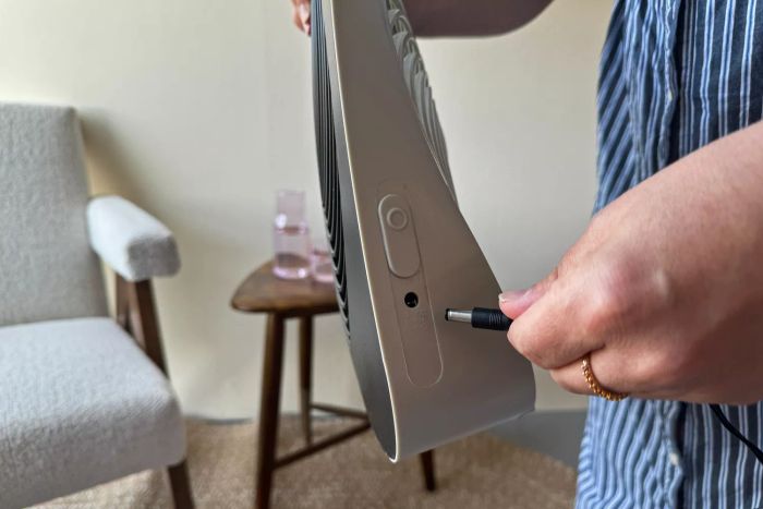 A person connects the Treva 10-Inch Portable Fan to an auxiliary cable.