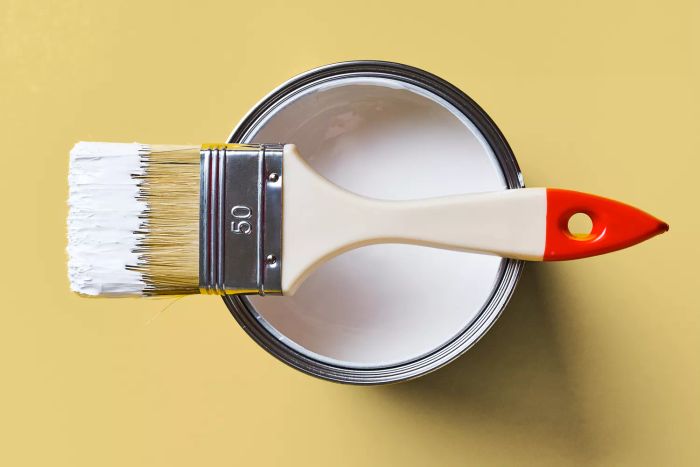 A jar of white paint brushed onto a bright yellow background. Painting and repair work.
