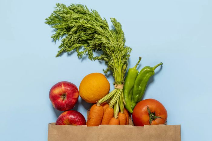 Bird's-eye view of a paper bag filled with fresh fruits and vegetables on a blue background