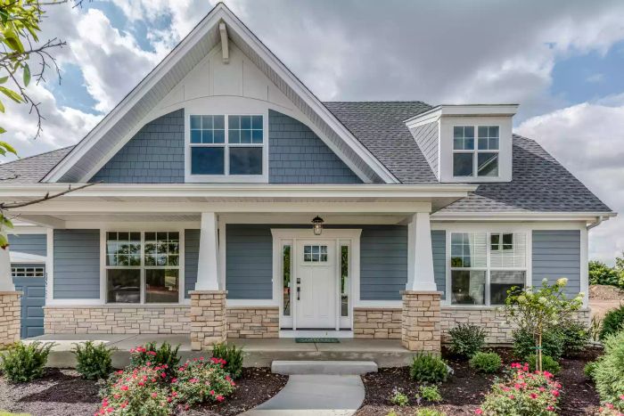A blue house featuring elegant stonework and a beautifully landscaped front yard