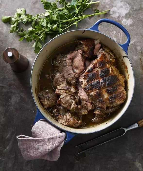 Slow-roasted lamb shoulder is taken out of the oven and served in a blue Dutch oven.