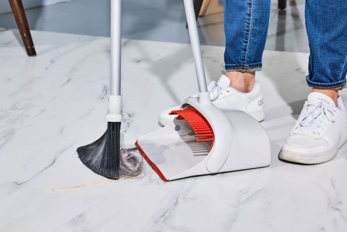 A person is using the OXO Good Grips Sweep Set with Extendable Broom to sweep dirt into the dustpan.