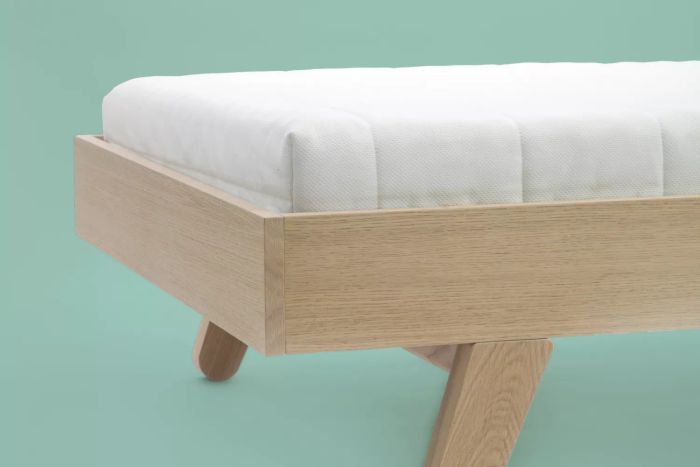 A mattress resting on a wooden platform bed with a green backdrop