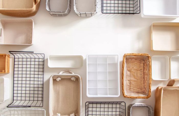 A top-down view of an organized closet featuring a variety of storage solutions, including shaped organization boxes and steel wire baskets, all neatly arranged on a white marble surface with plenty of space to spare. This includes Marie Kondo's hikidashi boxes for neatly folding clothes and drawer organization.