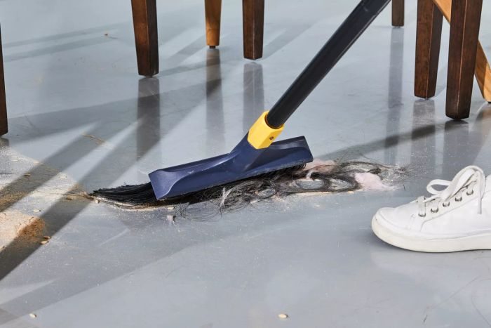 A person is cleaning up hair and dirt with the Yocada Heavy-Duty Outdoor Broom.