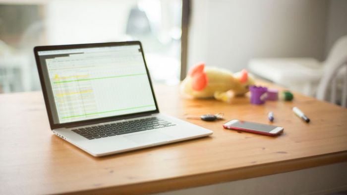 A laptop rests on a table surrounded by keys, toys, and a mobile device.