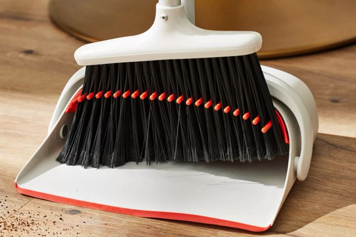 A person is using the OXO Good Grips Sweep Set with Extendable Broom to sweep dirt into the dustpan.