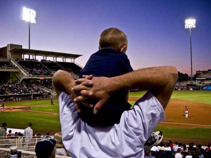 A father carrying his son on his shoulders at an Isotopes baseball game.