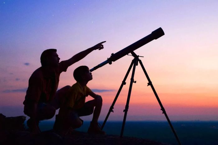 Father and son gazing through a telescope at dusk