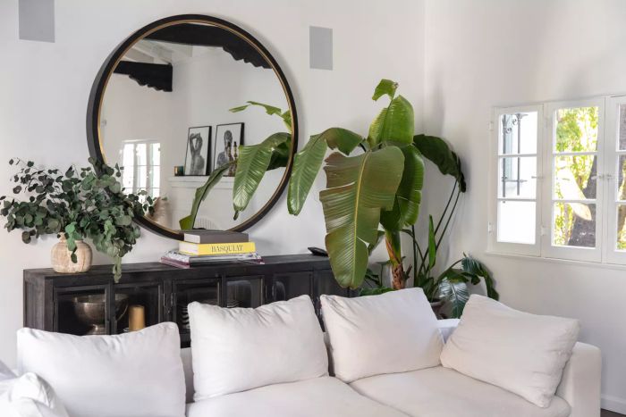 Round black-rimmed mirror above black cabinet and houseplants in living room