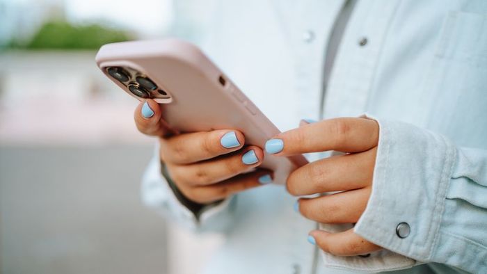 A close-up of a person with blue nails holding a smartphone