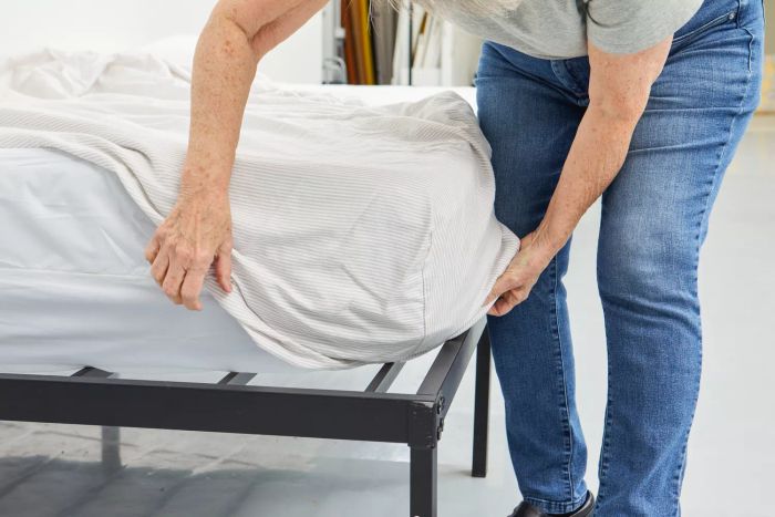 Person carefully tucking the corners of The Citizenry Organic Resort Cotton Sheet Set around the mattress