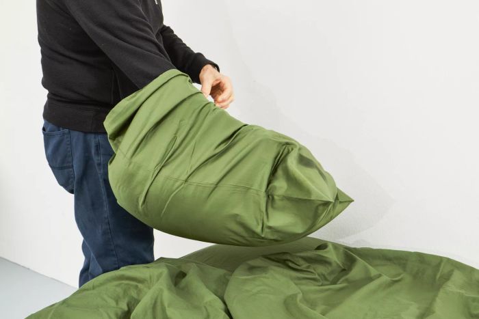 A person placing a pillow inside a pillowcase from the Nest Bedding Sateen Organic Cotton Sheet Set.