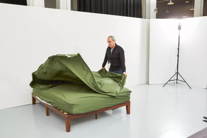 A person spreading Nest Bedding Sateen Organic Cotton Sheet Set on a bed.