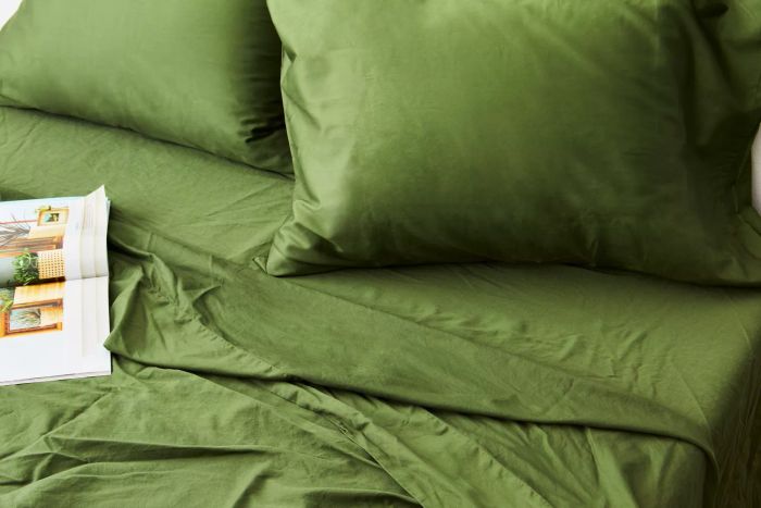 A close-up of a bed made with the Nest Bedding Sateen Organic Cotton Sheet Set, featuring a magazine placed on top.