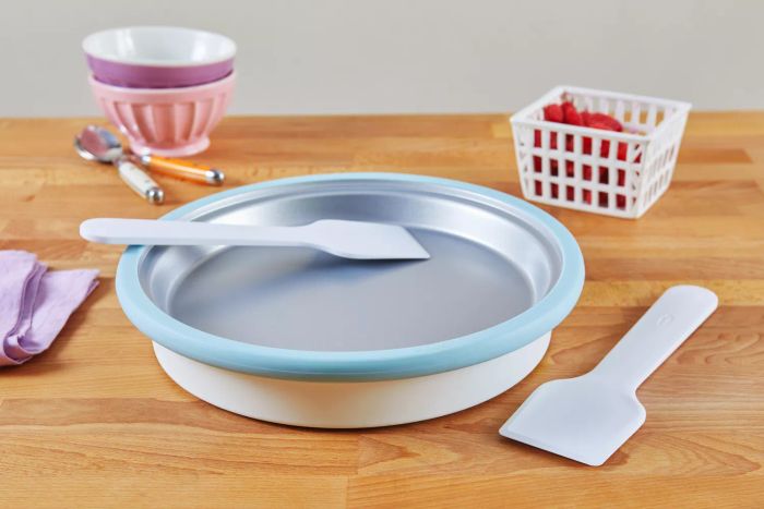 The Chef'n Sweet Spot Ice Cream Maker placed on a wooden surface alongside two bowls, a white basket, and two spoons.