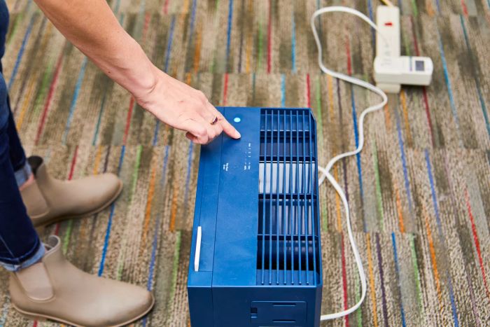 A finger pressing a button on the Coway Airmega 160 Air Purifier