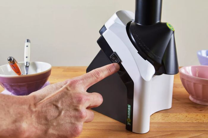 Hand pressing the power button on the Yonanas Classic Soft-Serve Dessert Maker