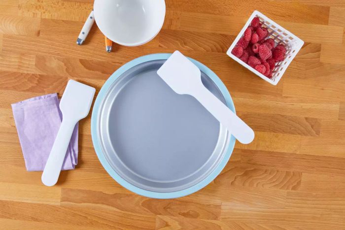The Chef'n Sweet Spot Ice Cream Maker set on a wooden surface next to two utensils and a basket filled with fresh raspberries.