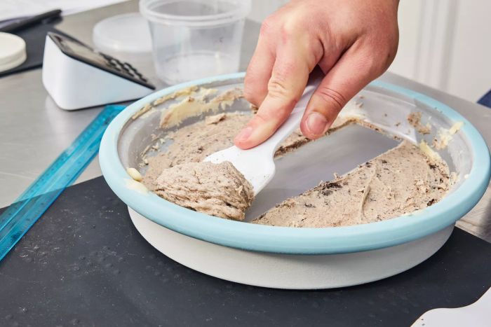 A hand uses a utensil to scrape ice cream from the Chef'n Sweet Spot Ice Cream Maker placed on a stainless steel surface.