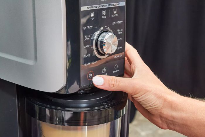 Close-up of a hand pressing the power button on the Ninja Creami Deluxe 11-in-1 XL Ice Cream Maker