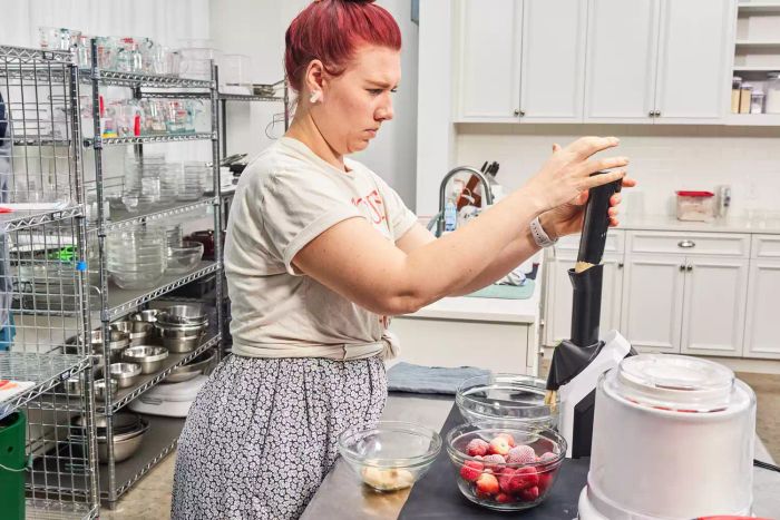Person holding the lid of the Yonanas Classic Soft-Serve Dessert Maker beside a bowl of frozen strawberries