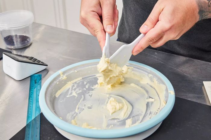 A person scrapes ice cream using utensils from the Chef'n Sweet Spot Ice Cream Maker set on a stainless steel surface.
