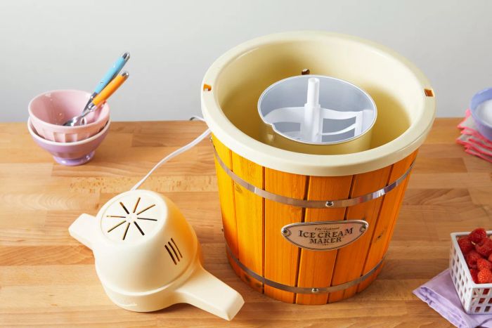 The Nostalgia 4-Quart Wood Bucket Ice Cream Maker placed on a wooden counter alongside bowls and spoons