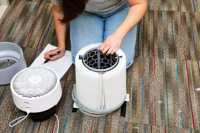 A person is assembling the Blueair Blue Pure 411i Max Air Purifier on a rug.