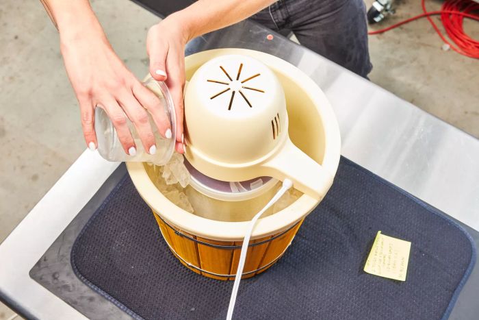 A person adding ice to the Nostalgia 4-Quart Wood Bucket Ice Cream Maker on a table