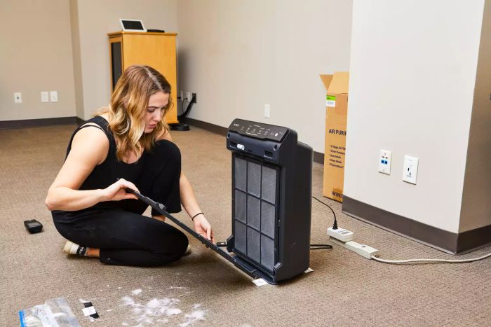 A person holds the front panel of the Winix 5500-2 4-Stage True HEPA Air Purifier.