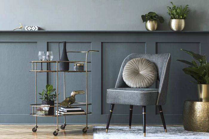 A living room designed with a chic armchair, wood paneling, potted plants, a bar cart, and other stylish home accessories.
