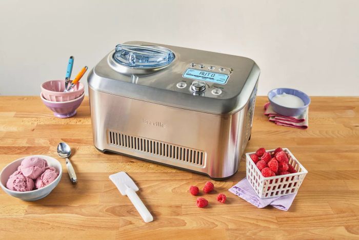 Breville The Smart Scoop Ice Cream Maker placed on a table beside fresh raspberries, bowls of ice cream, spoons, and other ingredients