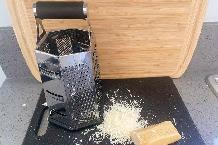 Utopia Kitchen Stainless Steel grater placed on a cutting board next to freshly grated cheese.