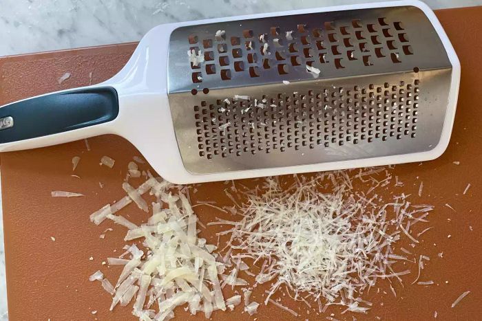 Zyliss Smooth Glide Dual Grater sitting on a cutting board with two small piles of grated cheese