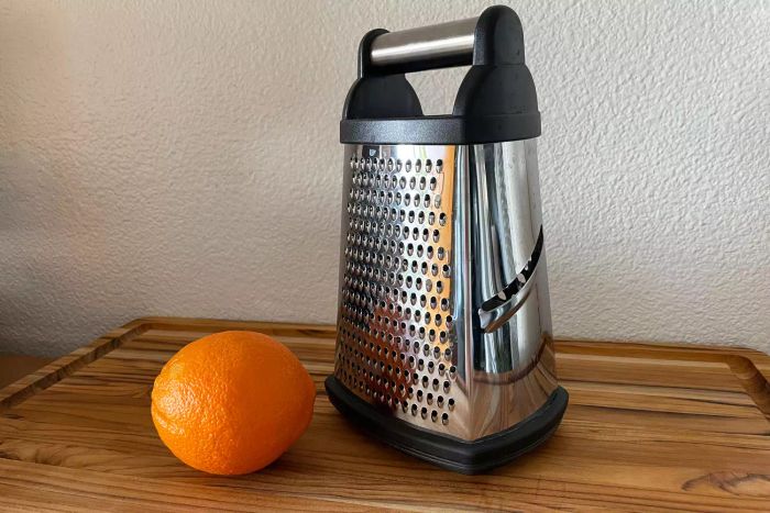 A recommended cheese grater resting on a wooden chopping board next to an orange