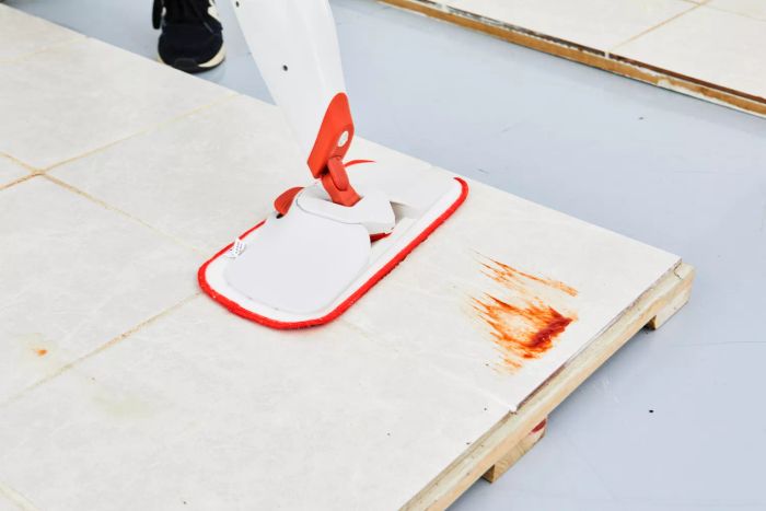 A close-up of the OXO Good Grips Microfiber Spray Mop in action, cleaning food debris off a tile floor.