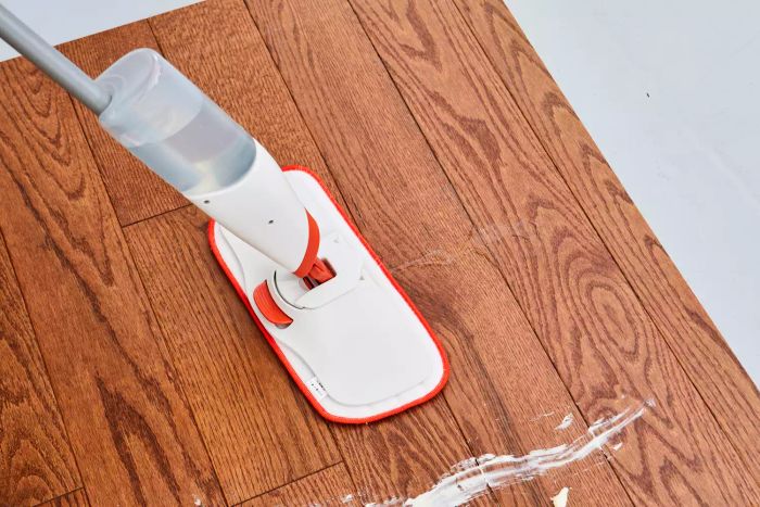 A close-up of the OXO Good Grips Microfiber Spray Mop in action, cleaning food spills from a wooden floor.