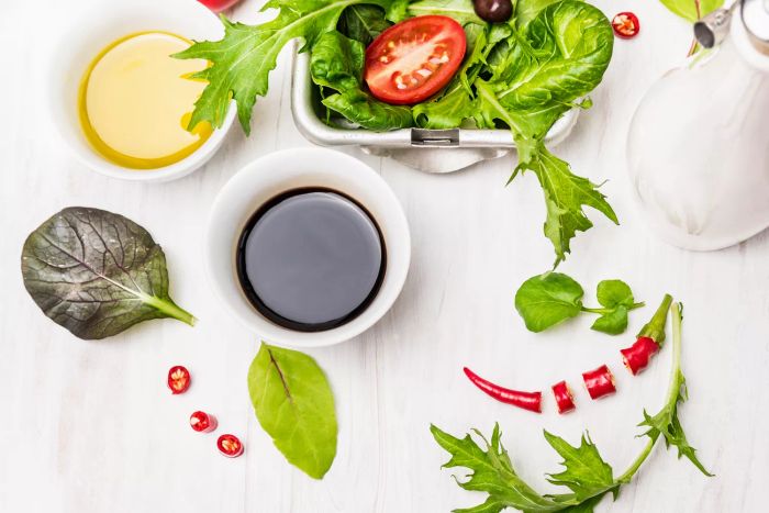 Salad prep featuring oil and balsamic vinegar on a white wooden surface