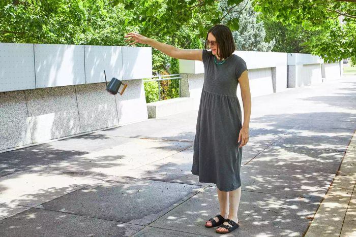 A woman attempting to carry the Terrain Beech Wood Handle Watering Can