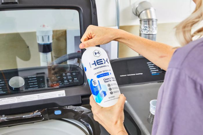 Person holding a bottle of HEX Performance Laundry Detergent in front of a washing machine