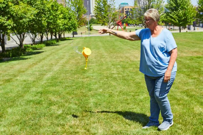Woman dropping the Haws Bosmere Handy Indoor Plastic Watering Can on the grass outside