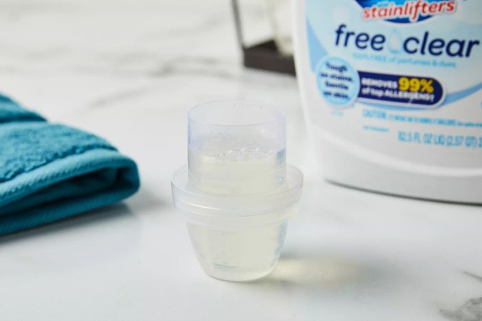 A filled cap of All Free Clear Liquid 2x Concentrated Laundry Detergent placed on a marble countertop.