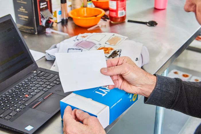 Hand holding a Bryt Laundry Detergent Sheet next to a box and a computer