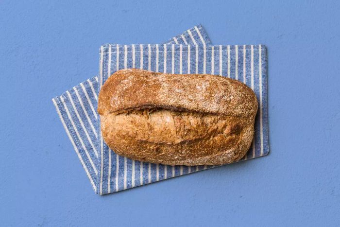 Homemade Whole Wheat Bread Freshly Baked. A loaf of bread resting on a napkin, with a rustic backdrop. A top view of the fresh bread.