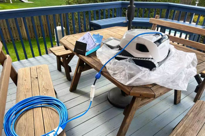 The pool cleaner, freshly removed from its packaging, resting on a picnic table surrounded by its plastic wrapping.