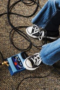 The guitarist's foot presses down on the pedal to activate different effects and transformations of sound.
